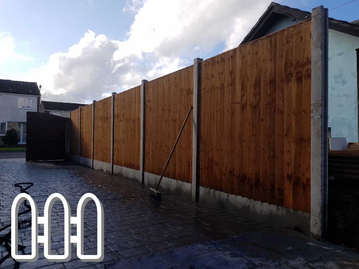 Newly installed tall wooden privacy fence in a residential driveway with dark clouds in the blue sky