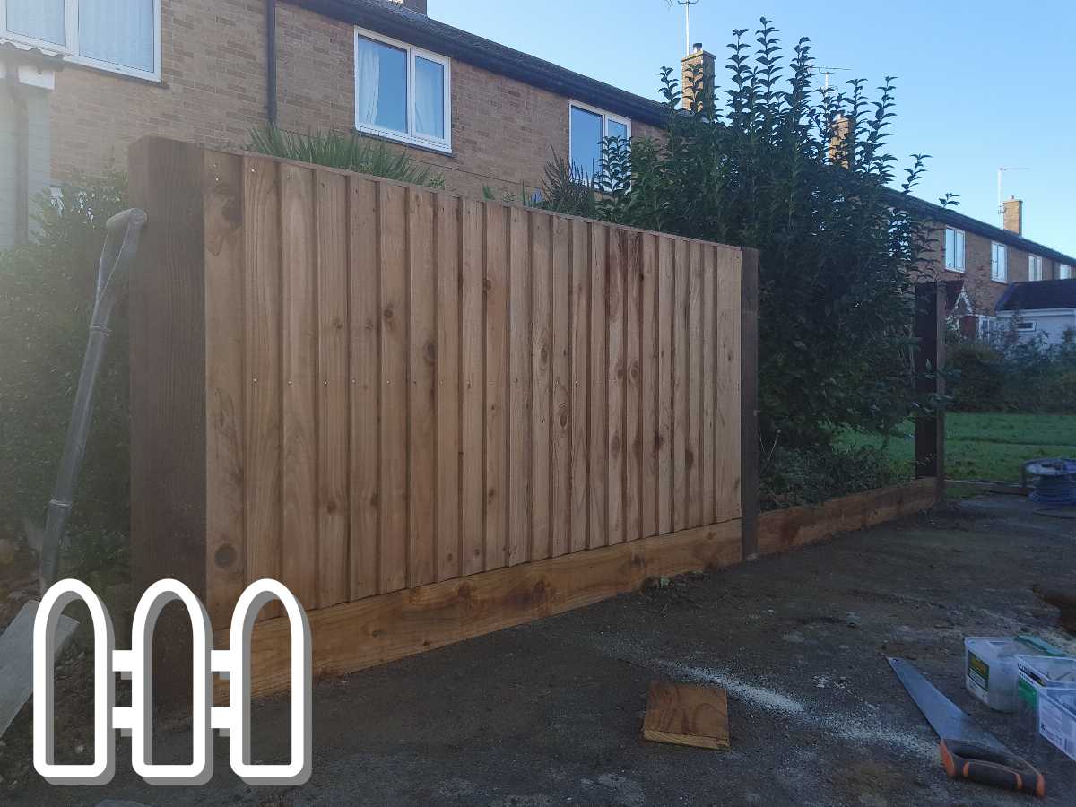 Newly installed wooden fence panel alongside residential building with construction tools visible on the ground