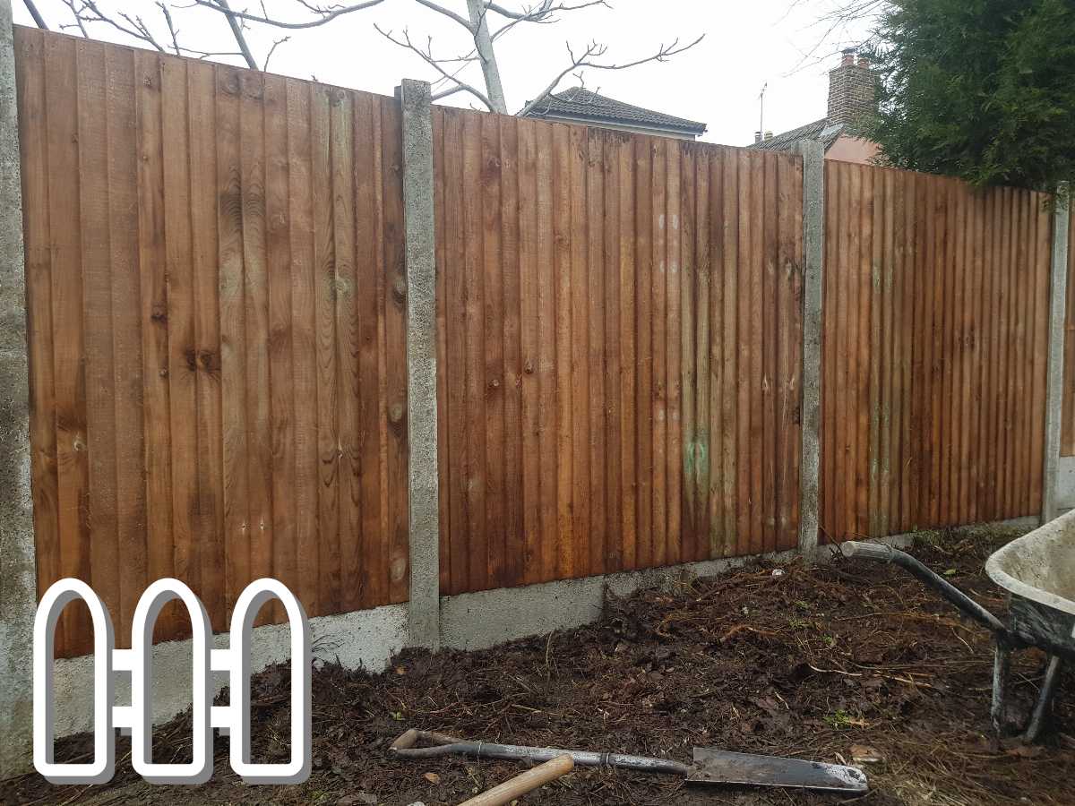 Newly installed wooden fence panels with concrete posts in a residential yard, with garden tools like a shovel and wheelbarrow in the foreground.