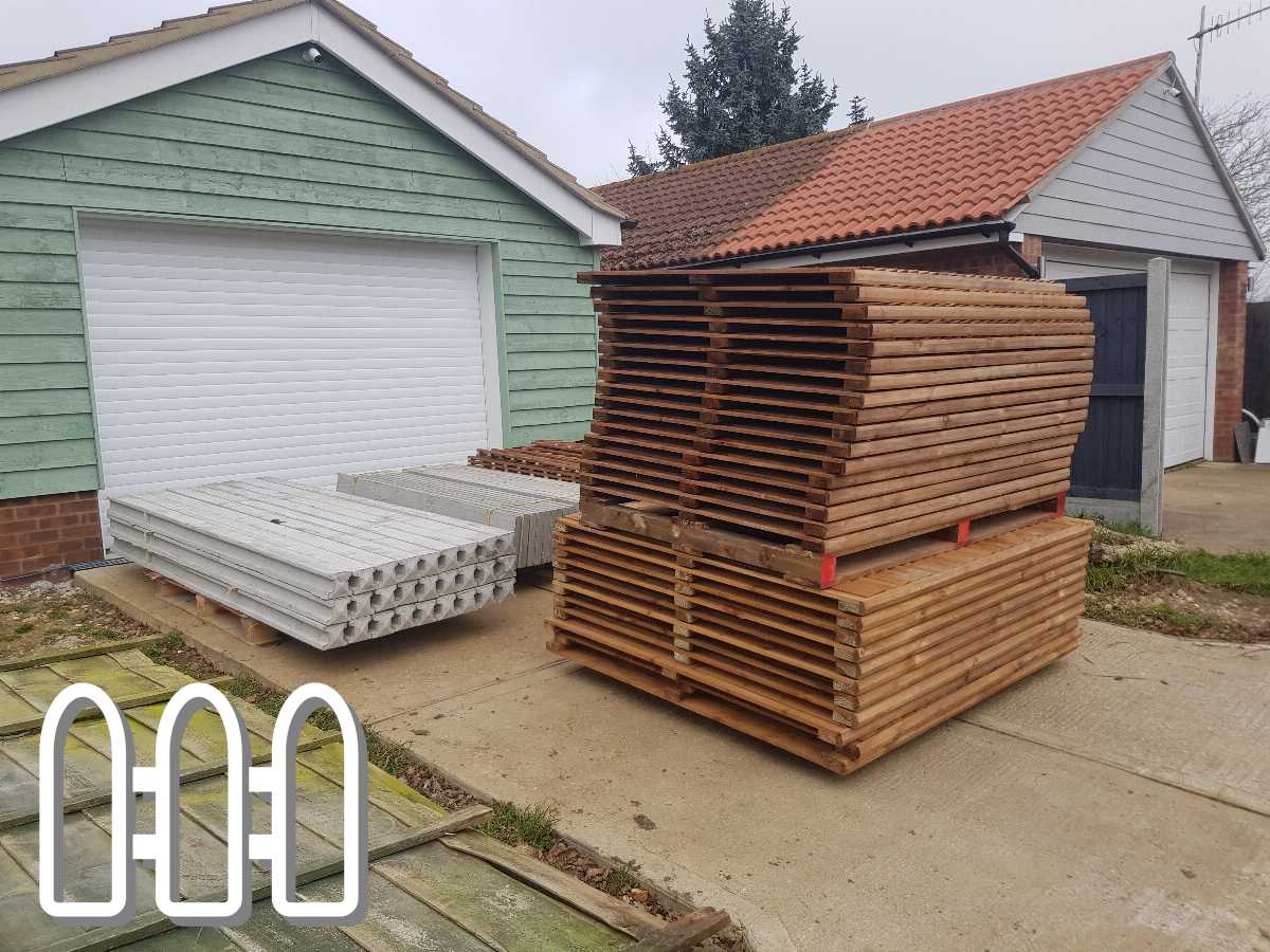 Stacks of fresh fencing panels and concrete posts ready for installation, arranged in a residential driveway near a green shed and a garage.