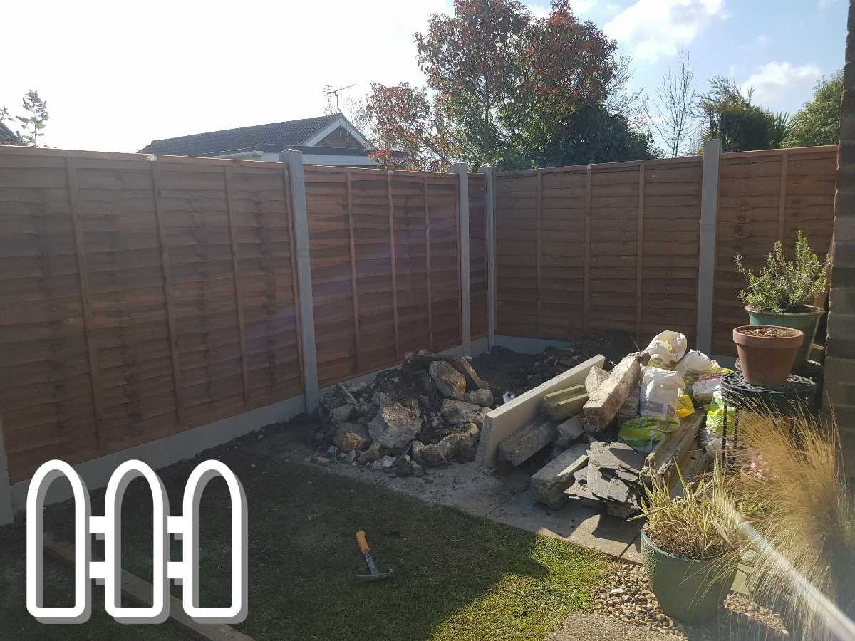 Newly installed wooden garden fence with concrete posts in a sunny backyard, construction debris and gardening tools scattered in the foreground.