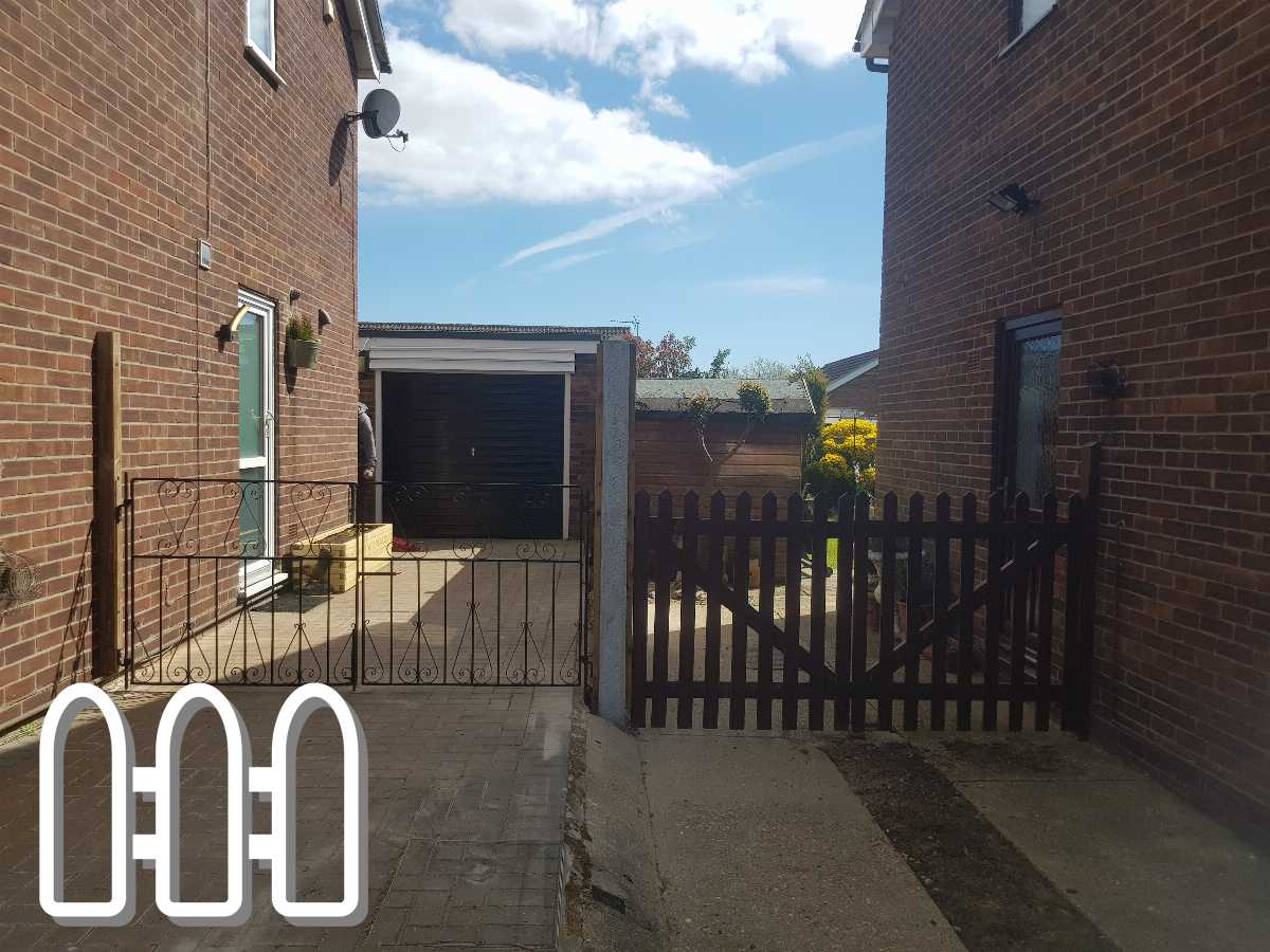 Residential outdoor area featuring ornate metal and wooden gates between brick buildings, with a clear blue sky overhead