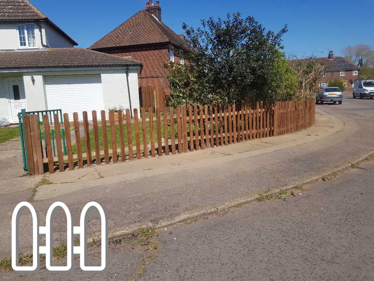 Wooden fence running along the edge of a driveway in a suburban neighborhood with a white house and garage in the background on a sunny day