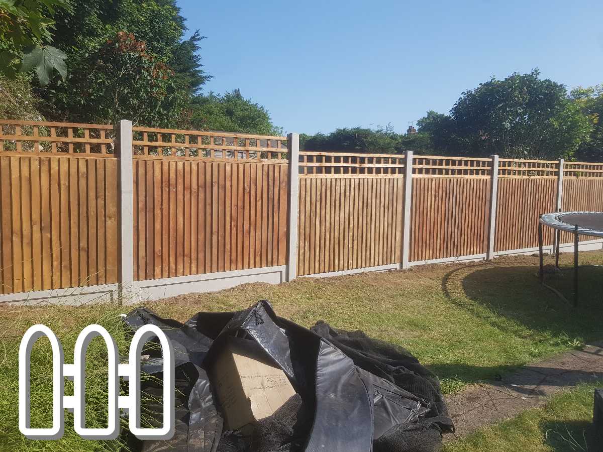 Newly installed wooden fence with concrete posts in a sunny backyard, showcasing detailed lattice work on top, adjacent to a garden with visible greenery and a discarded black tarp.