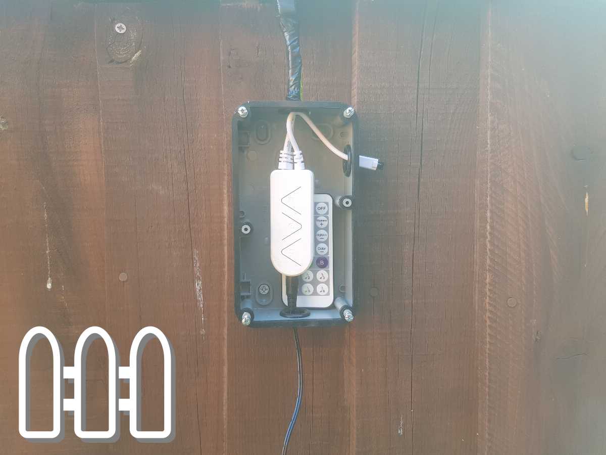 Outdoor electrical control box mounted on a wooden fence, with visible buttons and cable entry