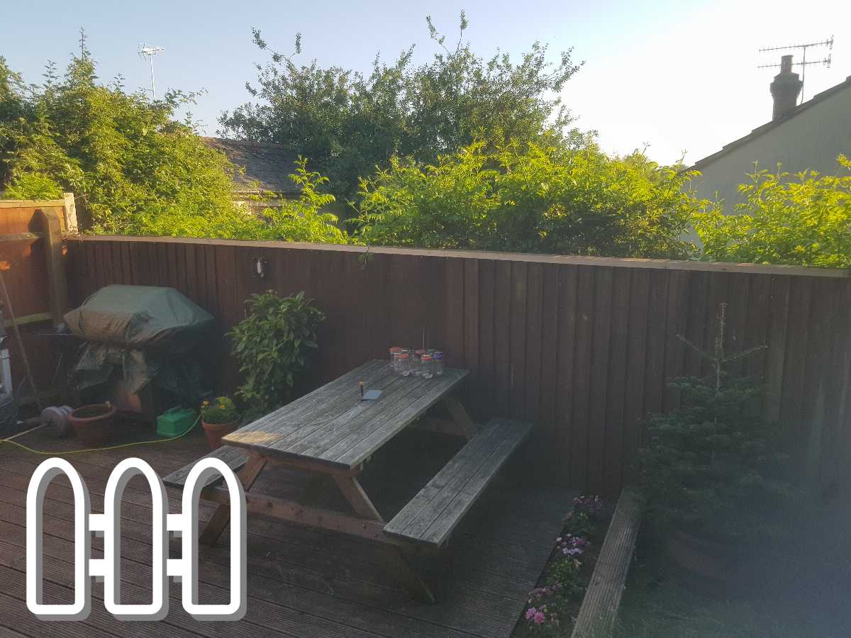 Tranquil backyard with a wooden fence, decking area featuring a picnic table, and a variety of green plants under sunny skies