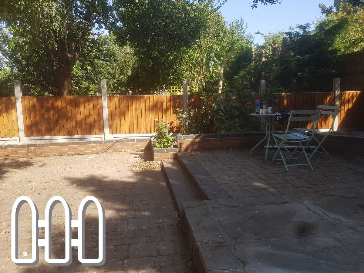 Tranquil backyard setting featuring a new wooden fence, brick planter beds, and a cosy outdoor seating area with a table and chairs on a flagstone patio.