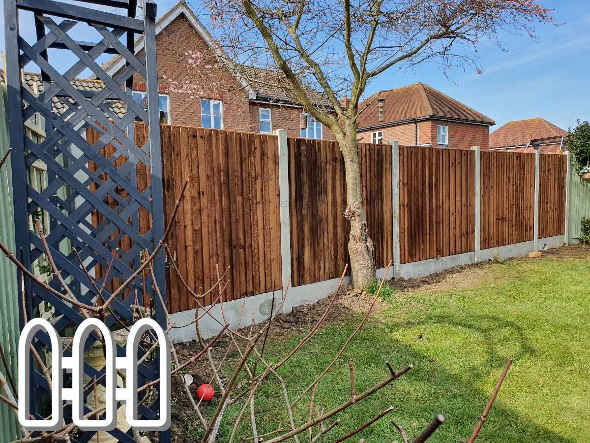 A sturdy wooden fence in a residential garden with houses in the background, featuring a green lawn and a small tree