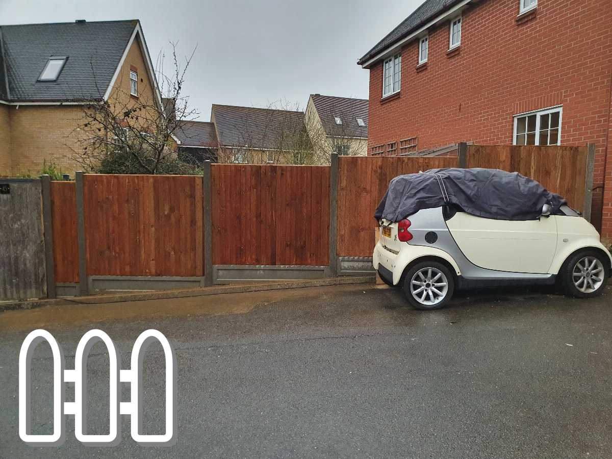Solid wooden fence in a residential area with a white convertible car covered with a black tarp parked beside it