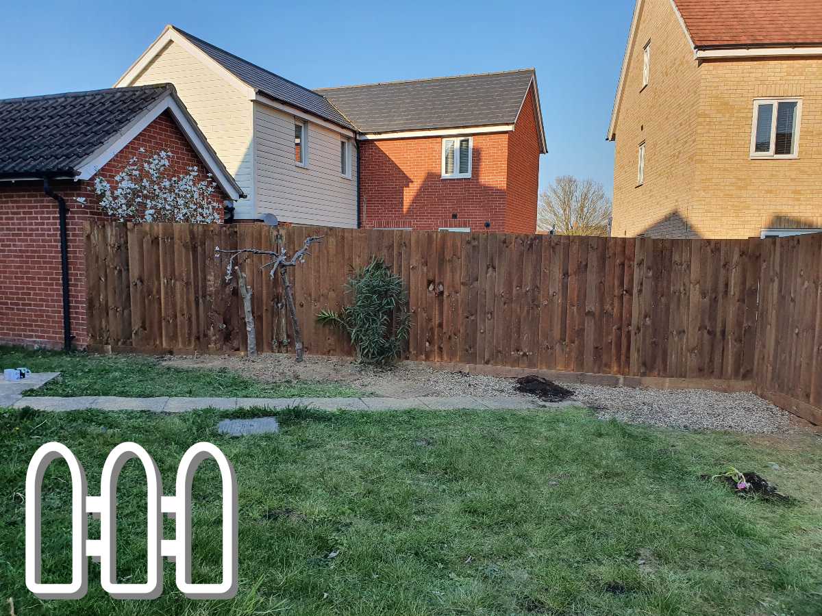 A sturdy wooden fence enclosing a backyard with a grassy lawn, a small tree, and a few plants, with modern houses in the background.