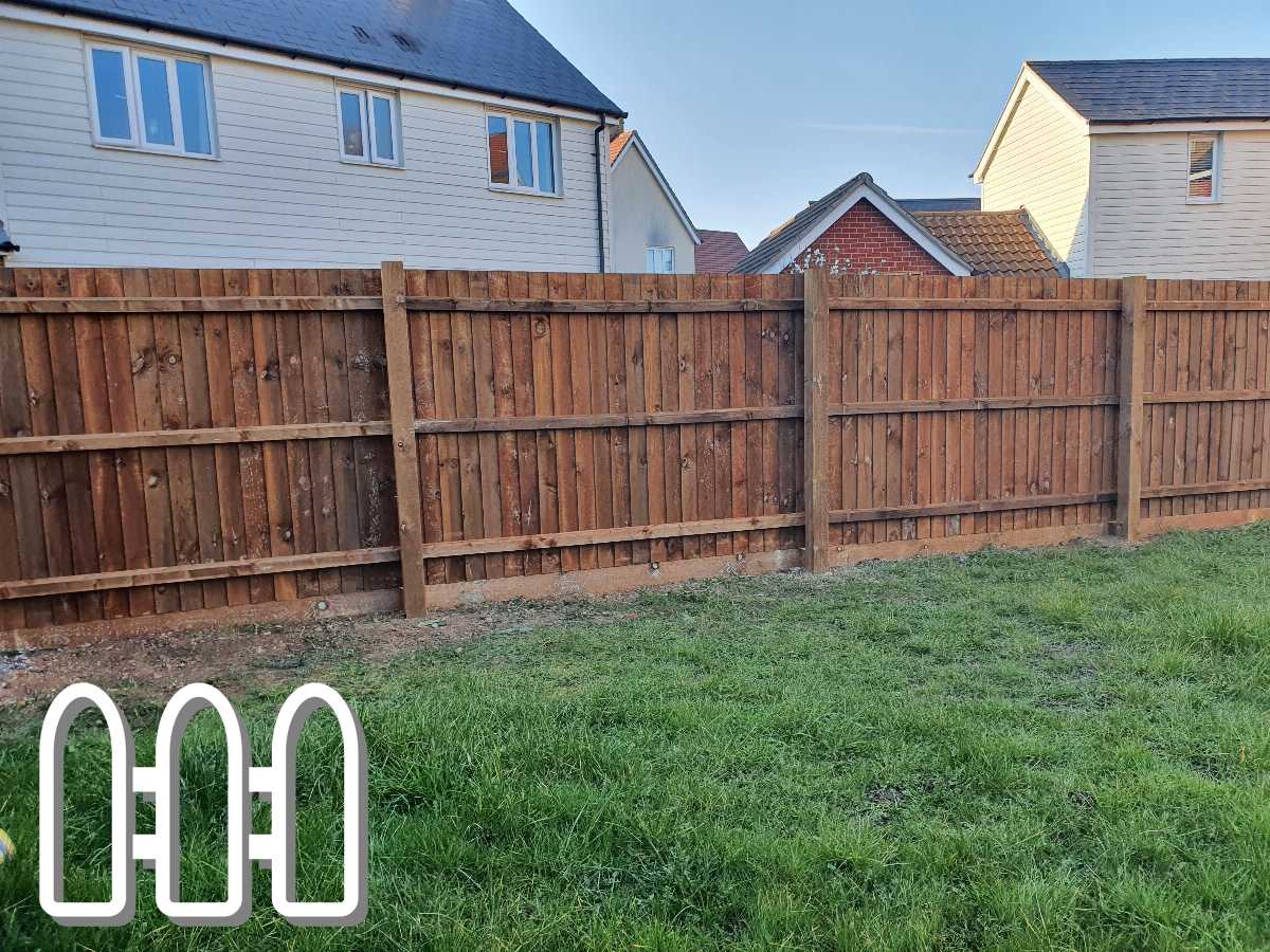 Wooden fence panels with vertical slats installed between homes in a residential area, with a view of grassy backyard and houses in the background.