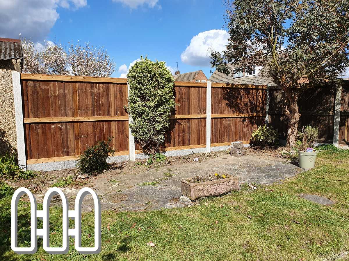 A well-maintained garden with a newly installed wooden fence under clear blue sky, featuring lush green grass, a paved stone area, and a variety of shrubs