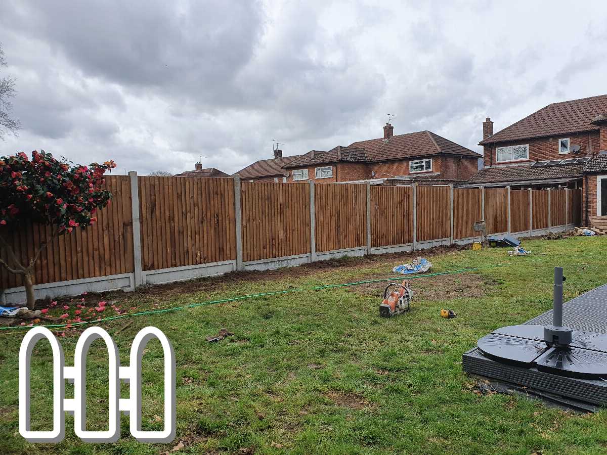 Newly installed wooden fence in a residential backyard with blooming camellia bush and construction tools scattered on grass