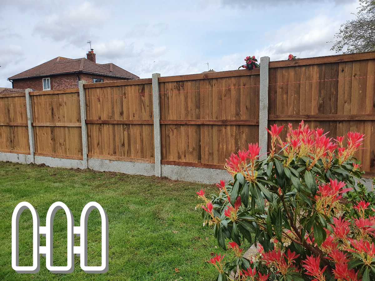 Wooden garden fence in pristine condition, featuring concrete fence posts and vibrant red flowers in the foreground, with a residential brick house in the background.