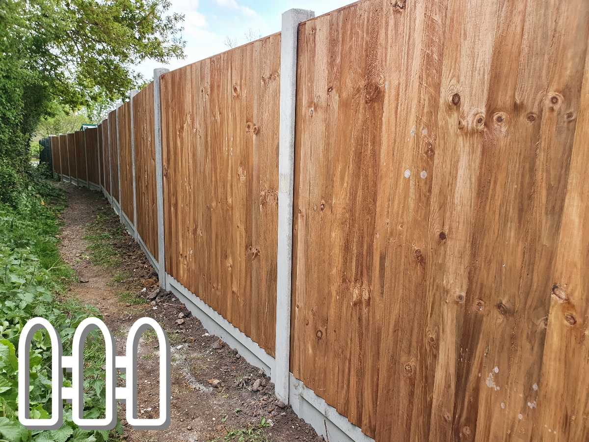 Durable wooden fence lining a narrow path, with a white concrete base, stretching into the distance surrounded by green foliage