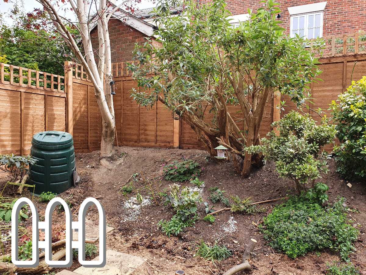 Well-maintained garden with a variety of plants and a compost bin next to a wooden fence and brick house