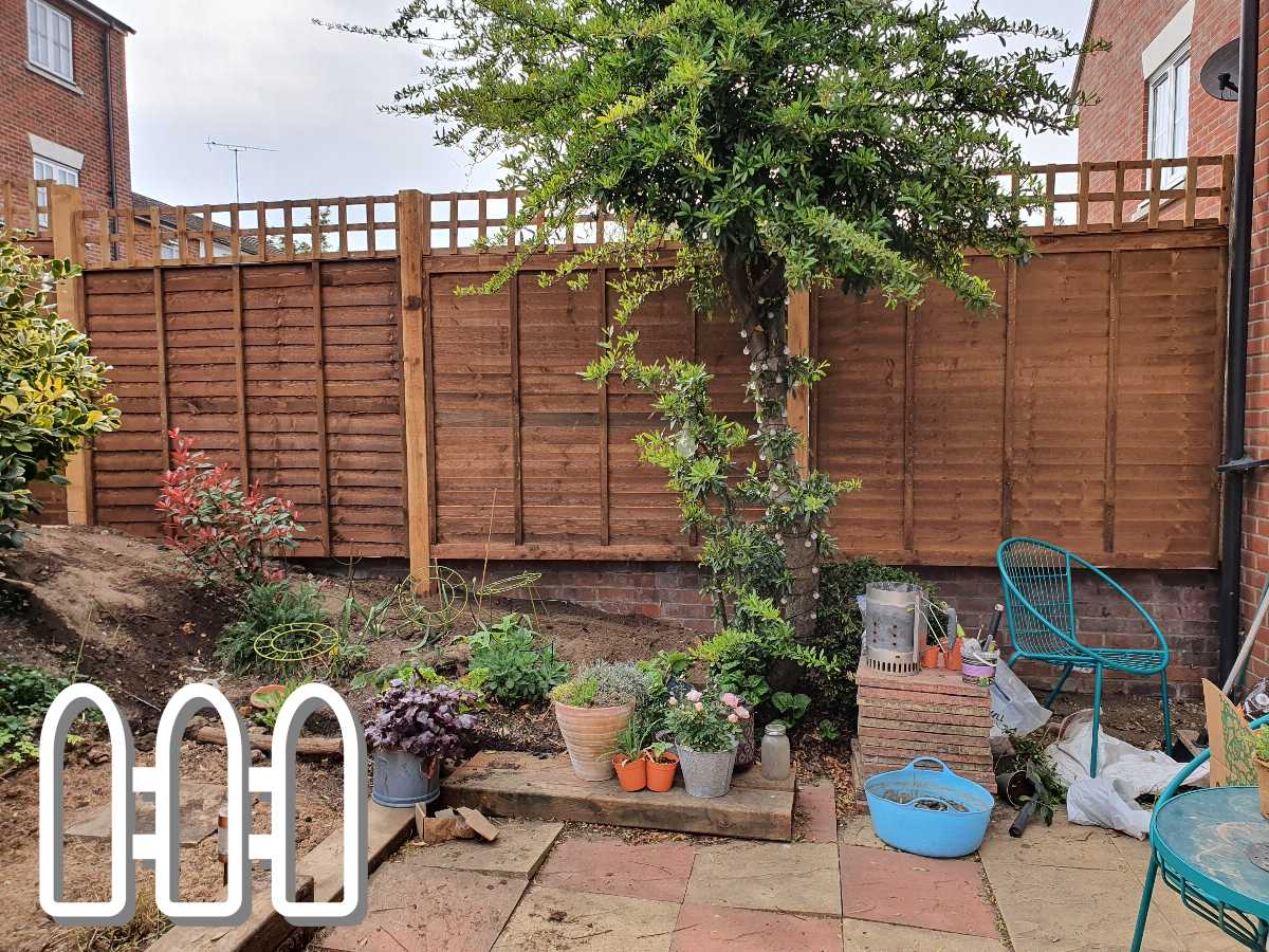 A newly installed wooden fence in a backyard with scattered gardening tools and plants, alongside a well-maintained tree near the house.